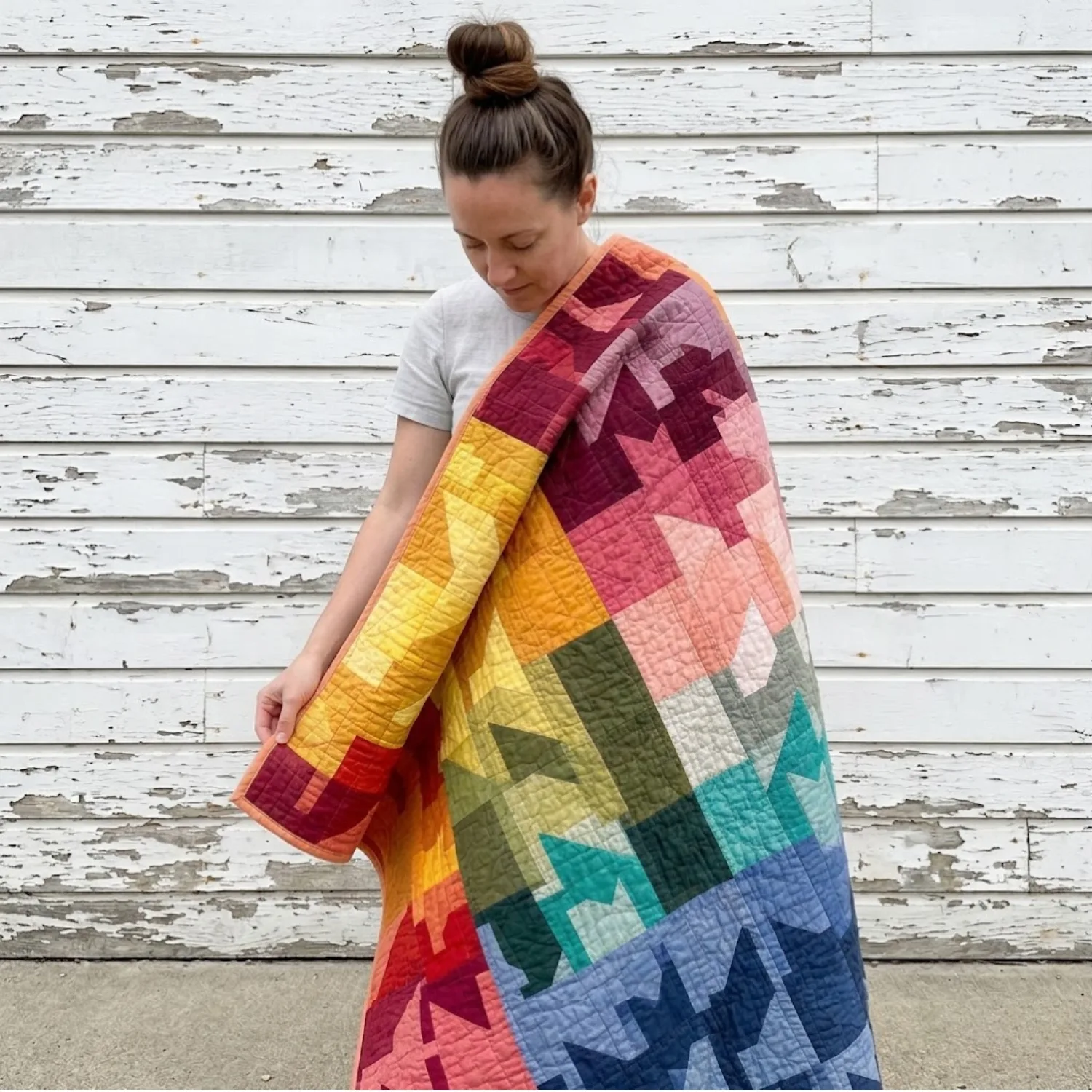 Woman holding a large colorful patchwork quilt — perfect upcycled fabric for the LU2COHOUSE Hooded Quilted Jacket sewing pattern